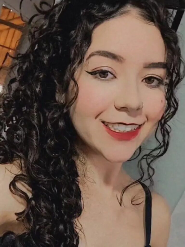 sou uma mulher branca de olhos castanhos claro e cabelos cacheados. Na foto me encontro de frente sorrindo e com óculos na cabeça além de uma blusa na cor azul escuro.