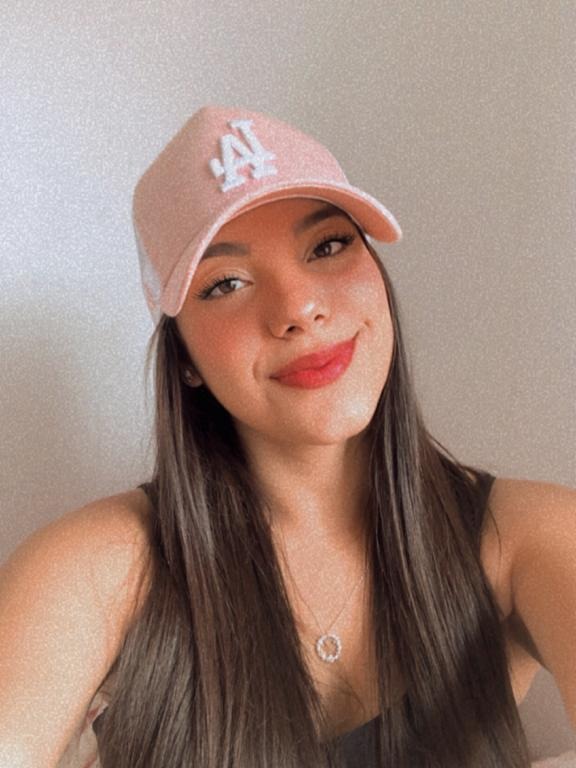 Sou uma mulher branca e estou de cabelo liso na foto (selfie), onde me encontro com uma blusa preta, cabelo solto e boné rosa.